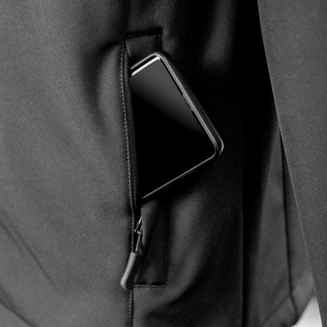 A black soft shell jacket with a smartphone partially tucked in the zippered side pocket.