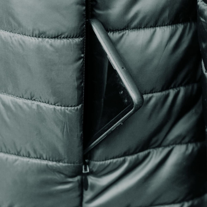 A black puffer jacket with a smartphone partially visible in the zippered pocket. The jacket features a quilted texture and has a logo.