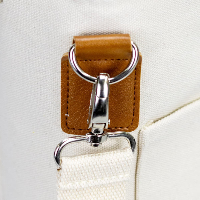 A close-up of a cream-coloured bag featuring a silver clip and a brown leather accent. The bag has a simple design.