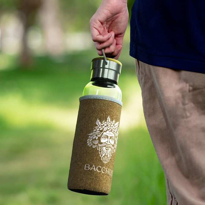 A drink bottle with a cork sleeve, featuring a metal lid, held by a person in a natural setting.