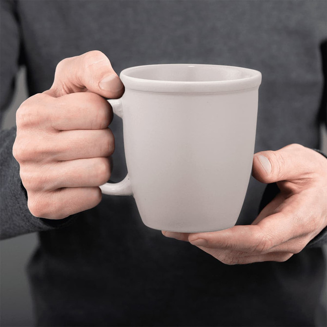 A ceramic mug in a light grey colour, held by a person with two hands. The mug has a smooth finish and a handle.