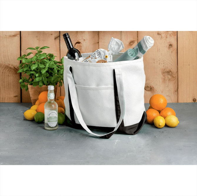 A white and black cotton tote bag filled with bottles, towels, and a potted plant on a surface with citrus fruits.