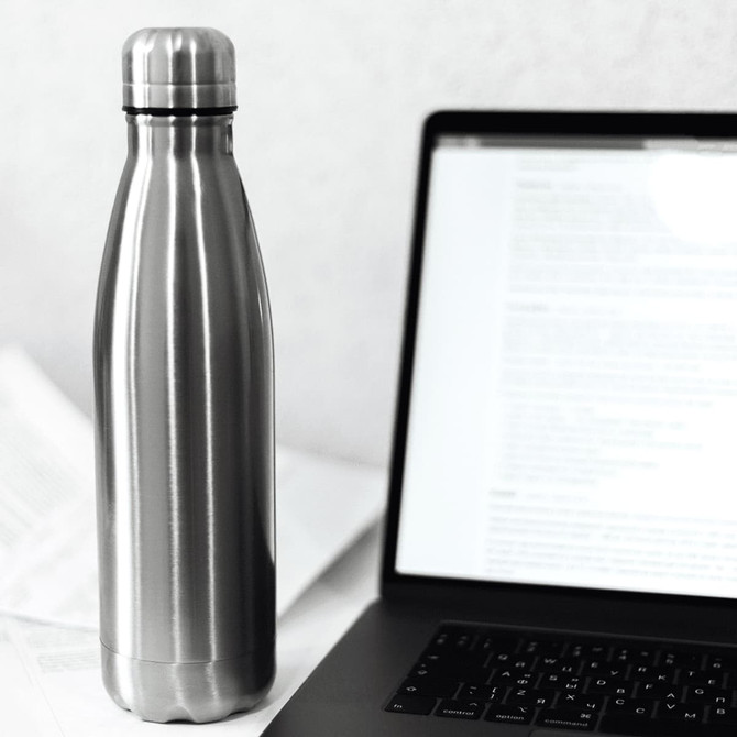 A drink bottle with a sleek stainless steel finish, featuring a logo, next to a laptop and papers.