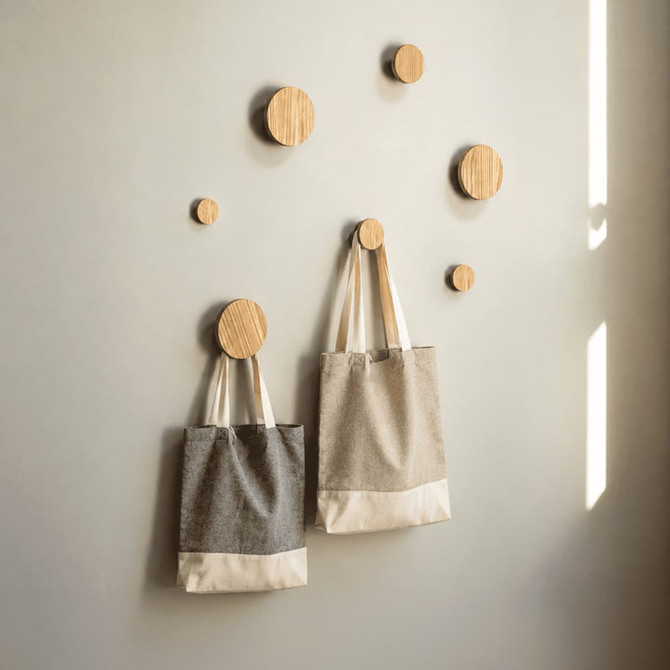 Two recycled cotton twill tote bags in grey and beige hanging on wooden pegs against a light wall.