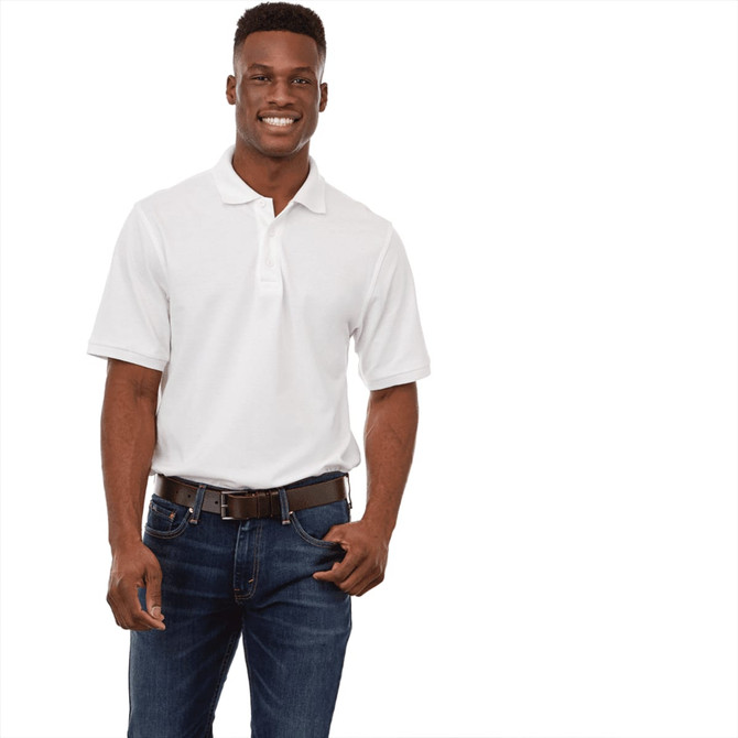 A man wearing a white short sleeve polo shirt paired with dark jeans, smiling and standing confidently. The polo features a logo.