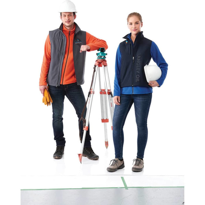 A grey and navy Stinson Softshell Vest for women displayed on a model, with a logo and safety gear.