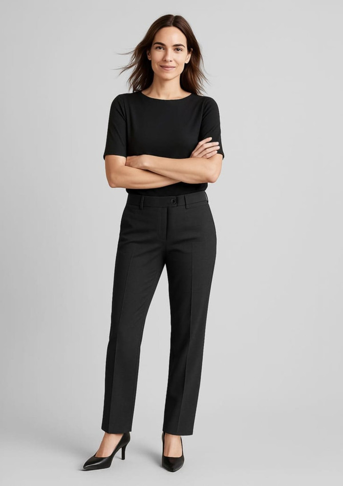A woman stands confidently in black relaxed pants paired with a black top and heels, featuring a subtle logo.