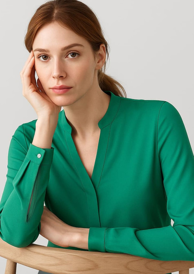 A green long sleeve blouse with a v-neckline and button details, displayed on a model sitting against a neutral background.