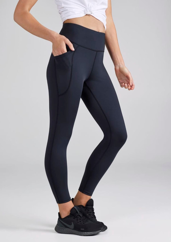 A pair of navy women's 7/8 length leggings with pockets, complete with a logo, worn with a white top and black shoes.