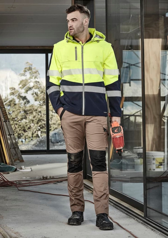 A man wearing a unisex two-tone softshell jacket in high visibility yellow and navy, paired with beige work trousers.