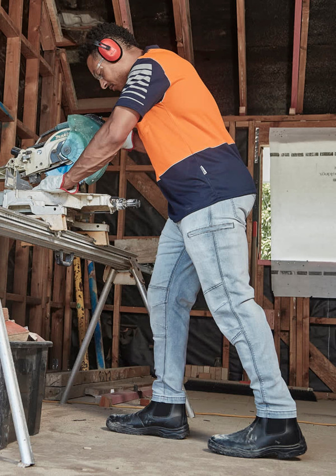 A man wearing men's stretch jeans in a light blue colour, working with a saw in a workshop environment.