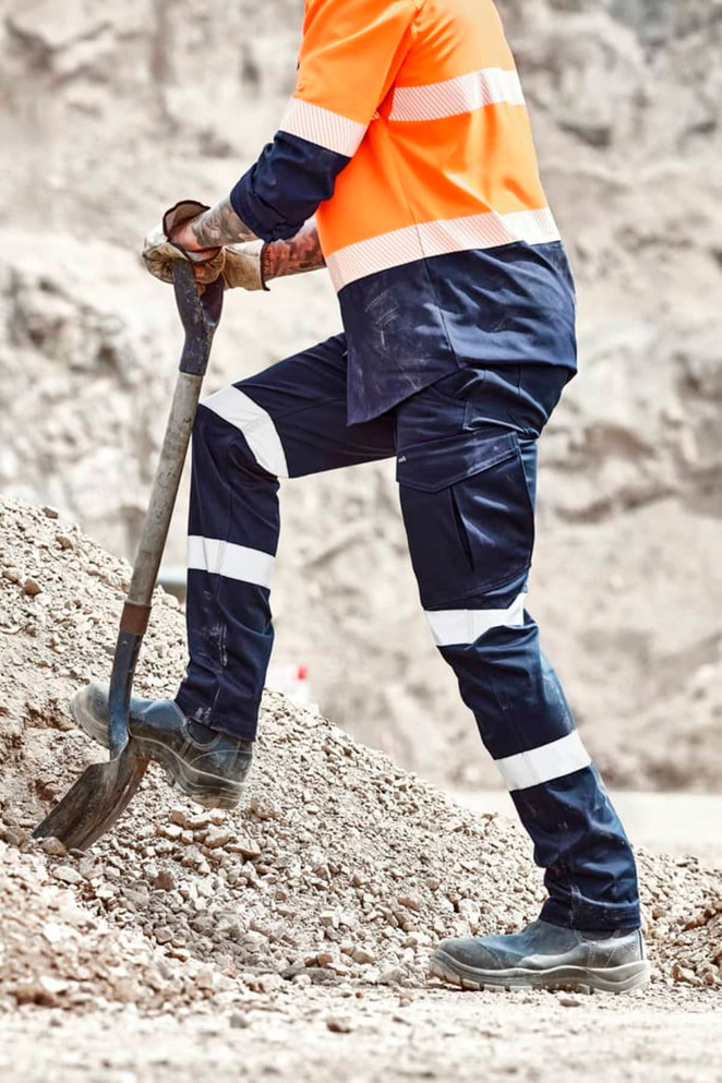 Mens essential stretch cargo pant in navy, featuring reflective stripes, worn with work boots and an orange high-visibility shirt.