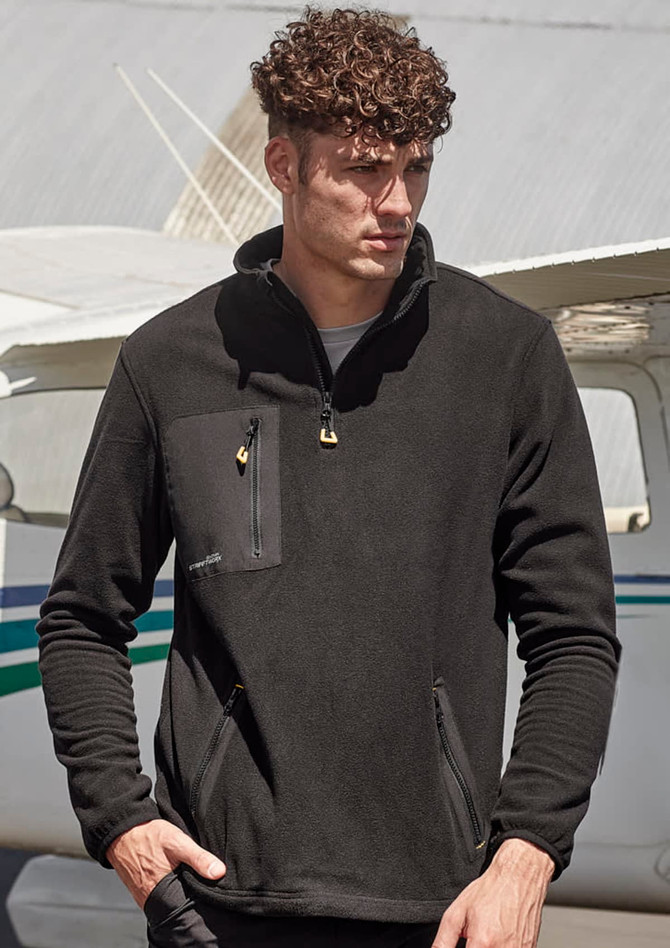 A man wearing a black unisex polar fleece with a quarter-zip and front pockets, set against an aircraft backdrop.