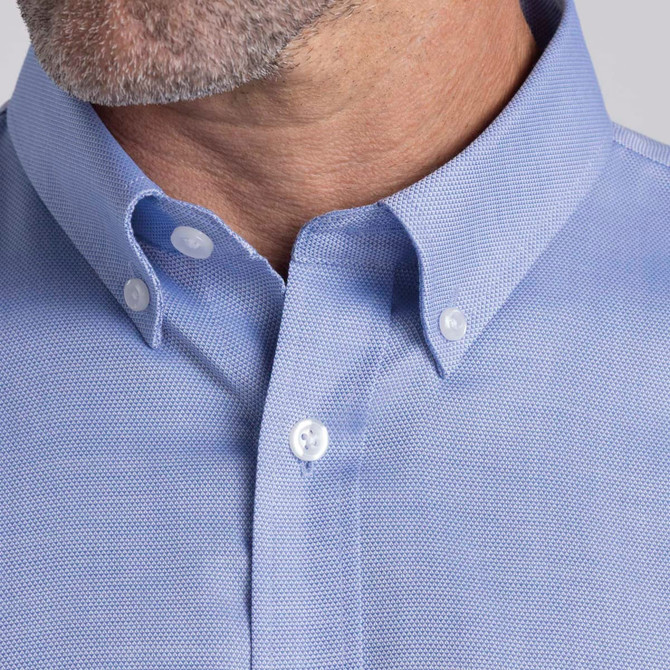 A close-up of a men's button-up shirt in light blue, featuring a pointed collar and buttons. It has a branding logo.