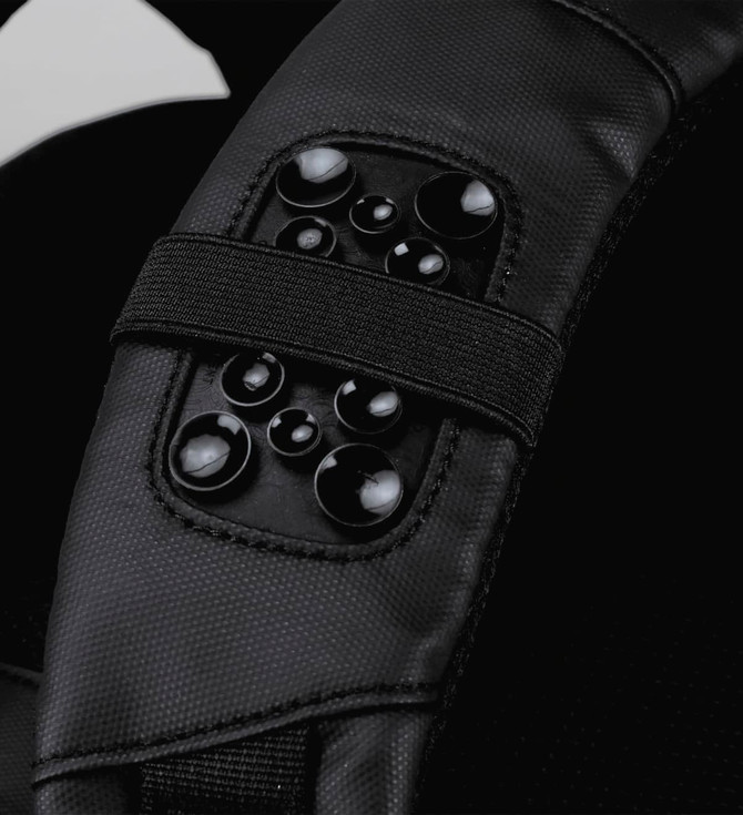 A close-up of a black backpack strap featuring a textured panel with multiple glossy round embellishments.
