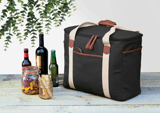 A black cooler bag with tan straps, surrounded by bottles of wine and beer, plus jars with snacks.