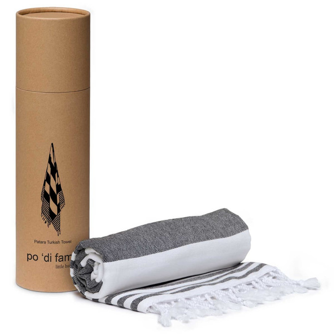 A rolled Patara Turkish towel in black and white, placed next to its cylindrical packaging.
