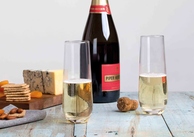 A bottle of champagne with two clear stemless flutes, set on a rustic table with cheese and snacks.