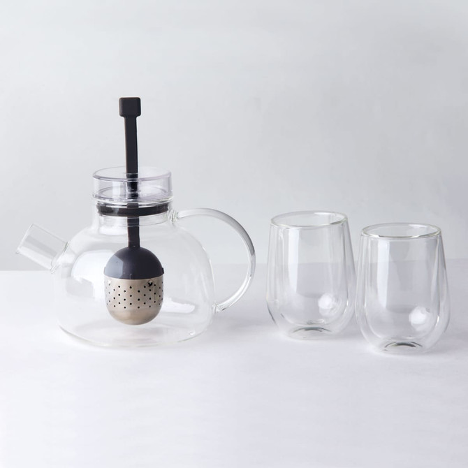 A glass teapot with a black infuser and two matching glass cups, all on a light surface.