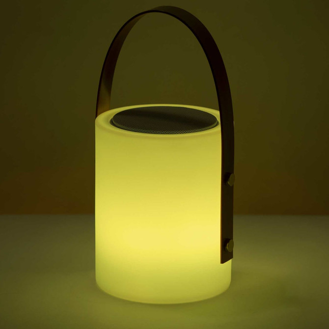 A lamp-shaped speaker in soft yellow with a metal handle and a speaker grating on top. It features a minimalist design.