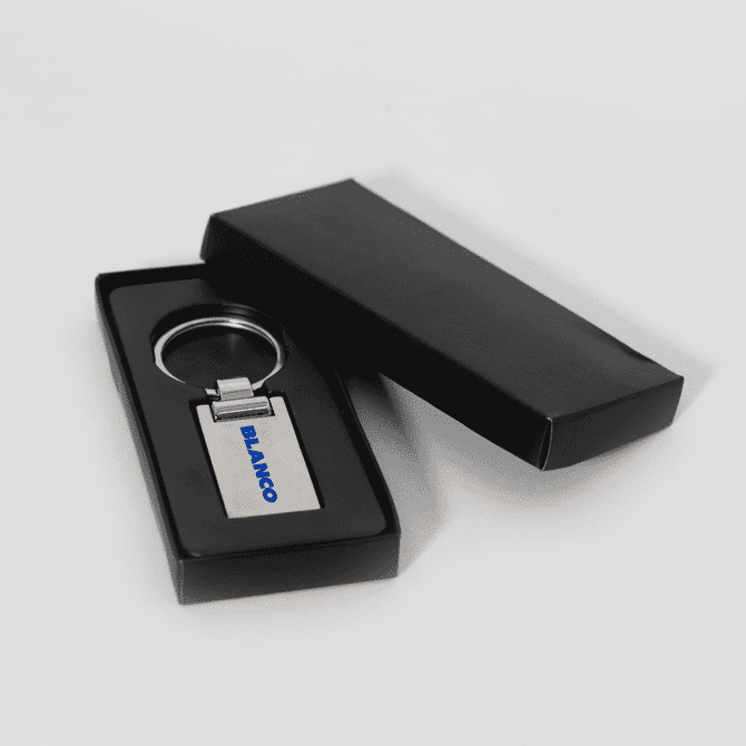 A silver keychain in a black presentation box, featuring a simple design and a logo.