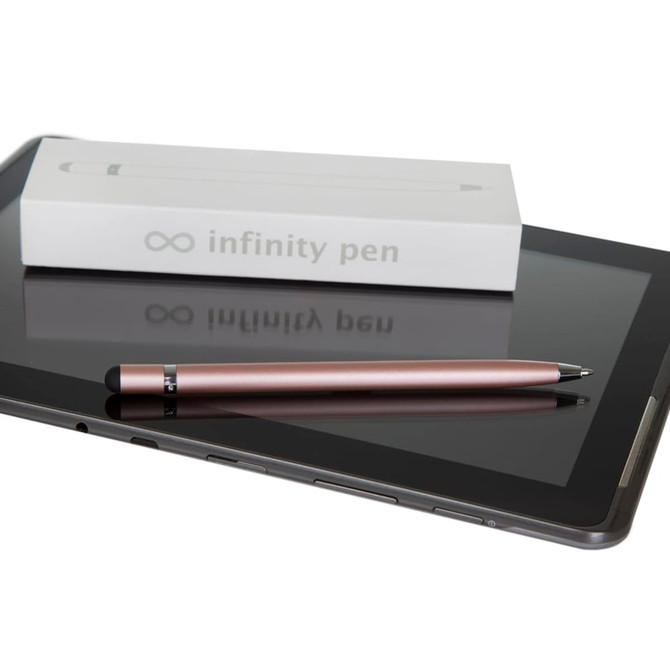 A metal Infinity Pen in rose gold rests beside a tablet and its packaging on a glossy surface.