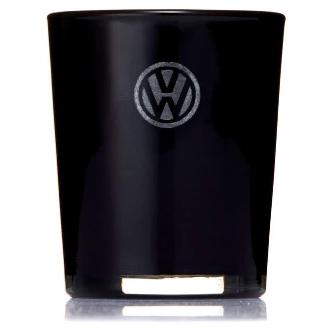 A black glass candle with a circular logo on the front, featuring a metallic base.