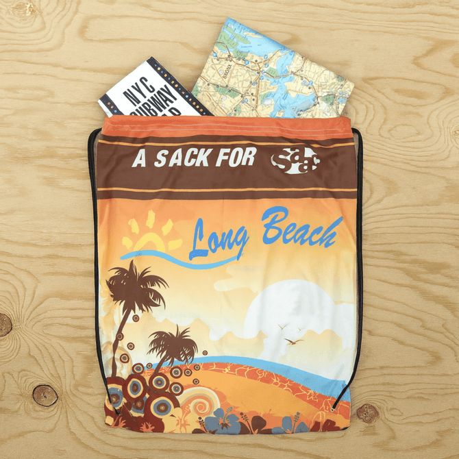 A drawstring backpack in vibrant orange, featuring a beach design, with a map and booklet peeking out from the top.