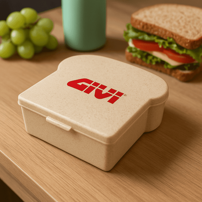 A beige wheat sandwich box with a logo, next to a sandwich and green grapes on a wooden table.