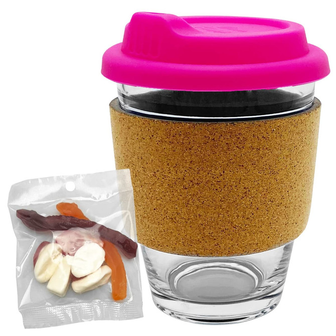 A glass coffee cup with a cork band and a bright pink lid, accompanied by a bag of mixed lollies.