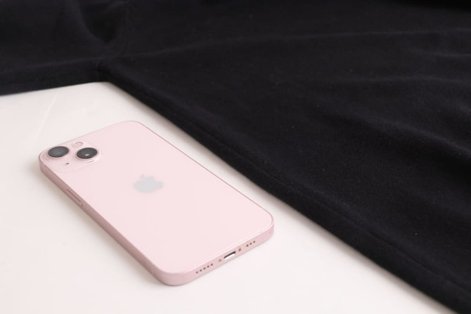 A black unisex cotton turtleneck sweater laid flat beside a pink iPhone. The sweater features a logo.