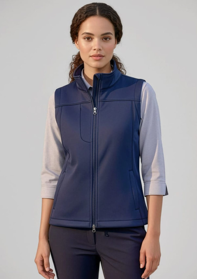 A women's softshell vest in navy blue, featuring a zip front and a collar, paired with a light long-sleeve top.