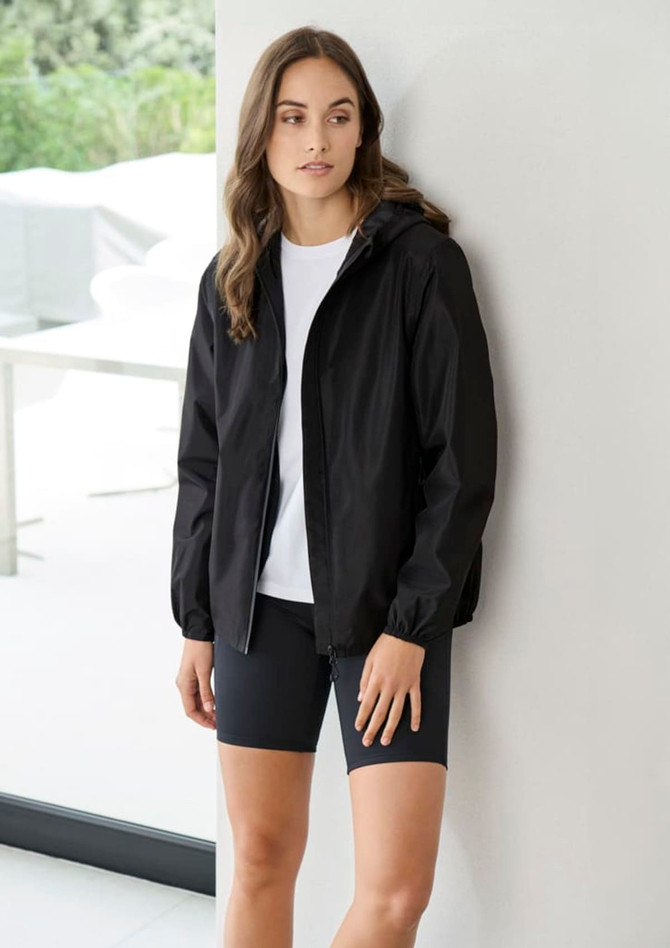 A women's black rain jacket with a hood, worn over a white shirt and black shorts, displayed indoors.