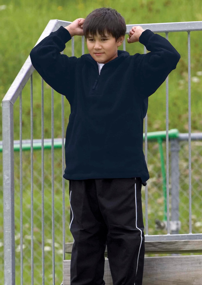 A boy wearing a black detailed polar fleece pullover stands on a metal structure, with green grass in the background.