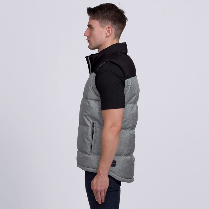 A grey puffer vest with a black collar, featuring a logo and side pockets, worn by a model in profile.