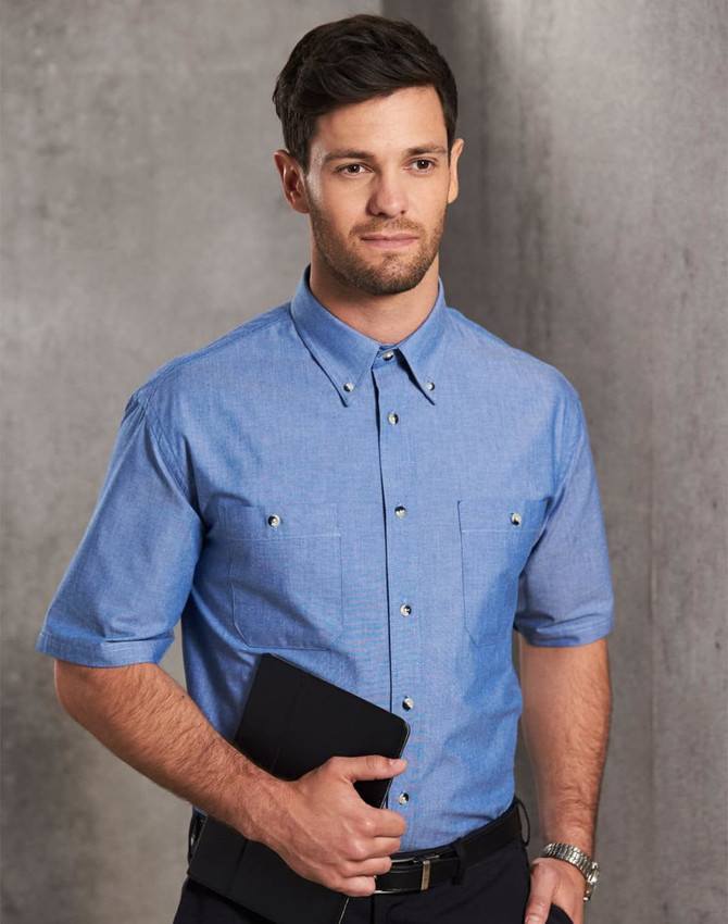 A man wearing a short sleeve chambray shirt in light blue, holding a folder. The shirt features a classic button-up design.