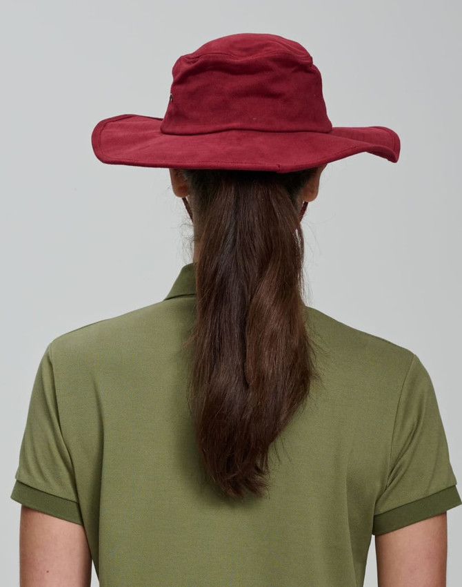A maroon surf hat viewed from the back, worn by a person with long brown hair, paired with an olive green shirt.
