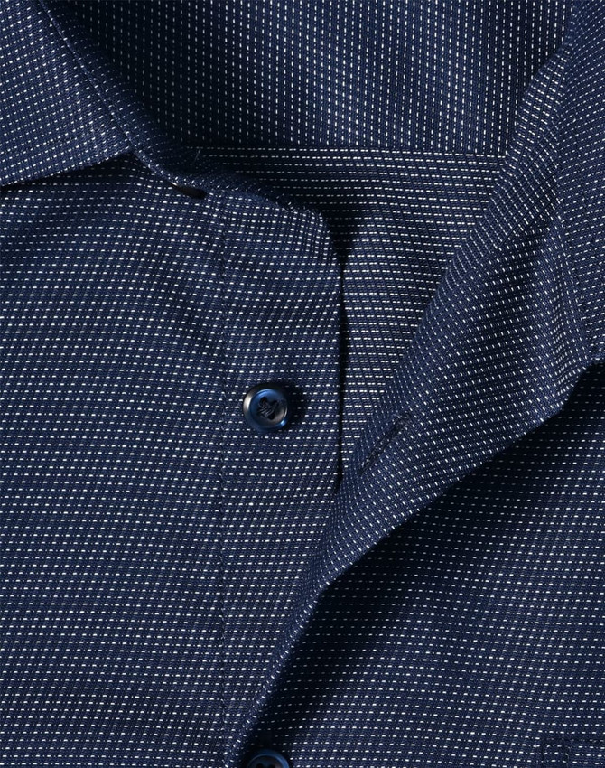 A close-up of a navy blue men's button-up shirt featuring a pin dot pattern and a collar with buttons.