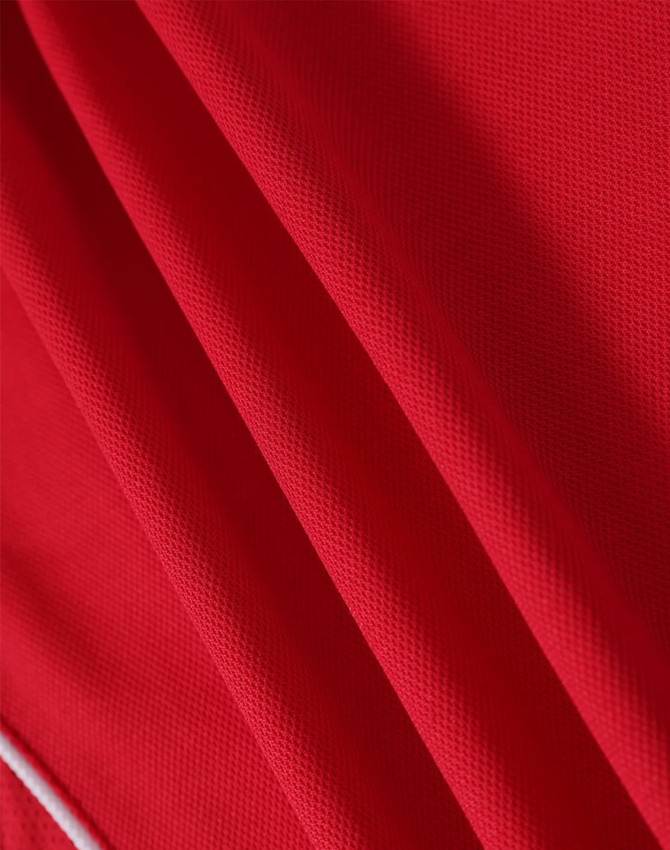 A red polo shirt made from a textured fabric, featuring a subtle branding logo.