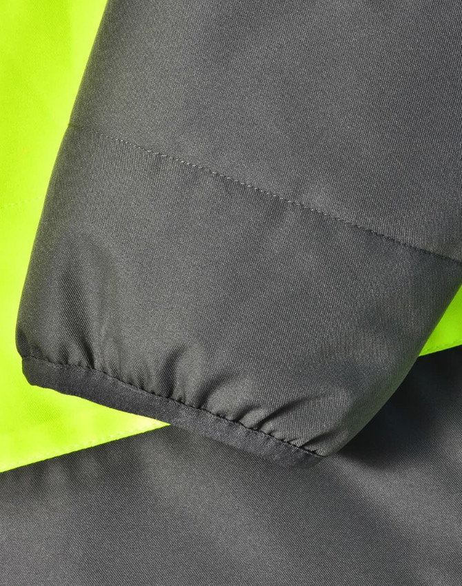 A close-up of a two-tone safety jacket featuring fluorescent yellow and charcoal grey fabric. It has a textured finish and elastic cuffs.