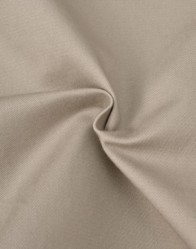 A close-up of beige cotton stretch drill fabric, showcasing its smooth texture and subtle sheen.