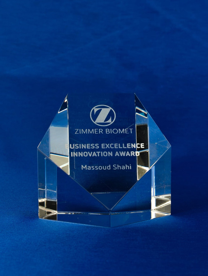 A clear crystal pentagon paperweight with an engraved award, displayed on a blue background. It has a logo and text.