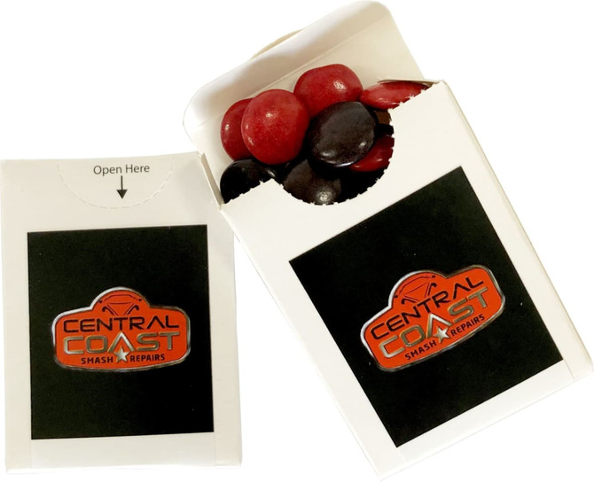 A branded flip lid cardboard box containing red and black choc beans, featuring a logo on the front.