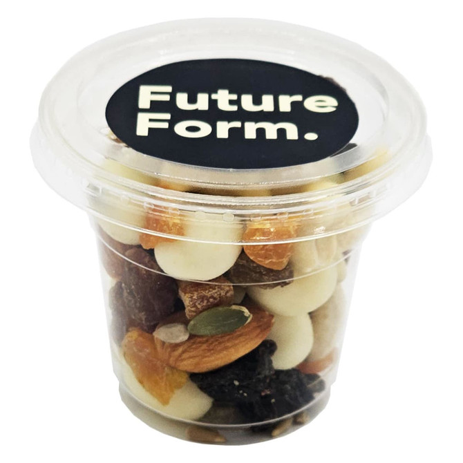A clear tub filled with a mix of yoghurt-coated nuts, dried fruits, and seeds. The lid features a logo.