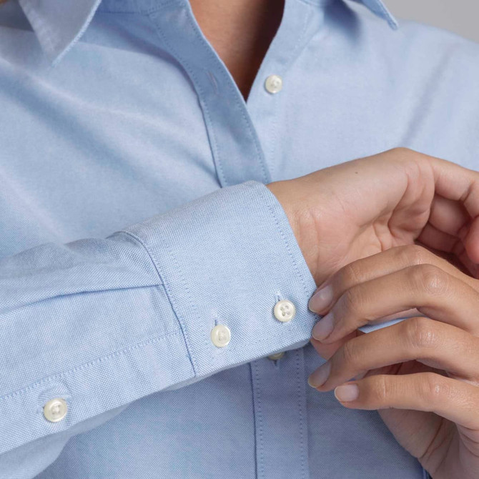 A light blue button-up shirt with a single cuff and buttons on the sleeves, featuring a branded logo.