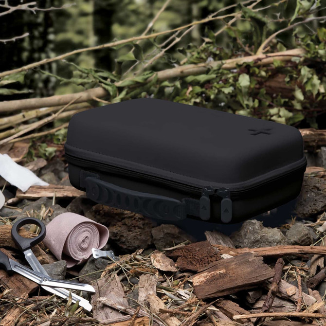 A black first aid kit resting on natural foliage, surrounded by a pair of scissors and a rolled bandage.