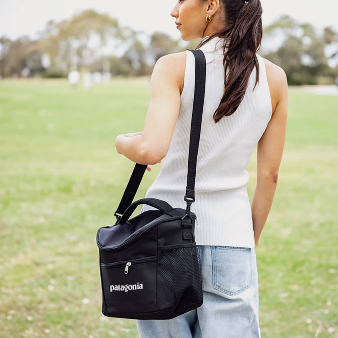 A black cooler bag with a shoulder strap and mesh pocket, being carried by a person in a casual outfit.