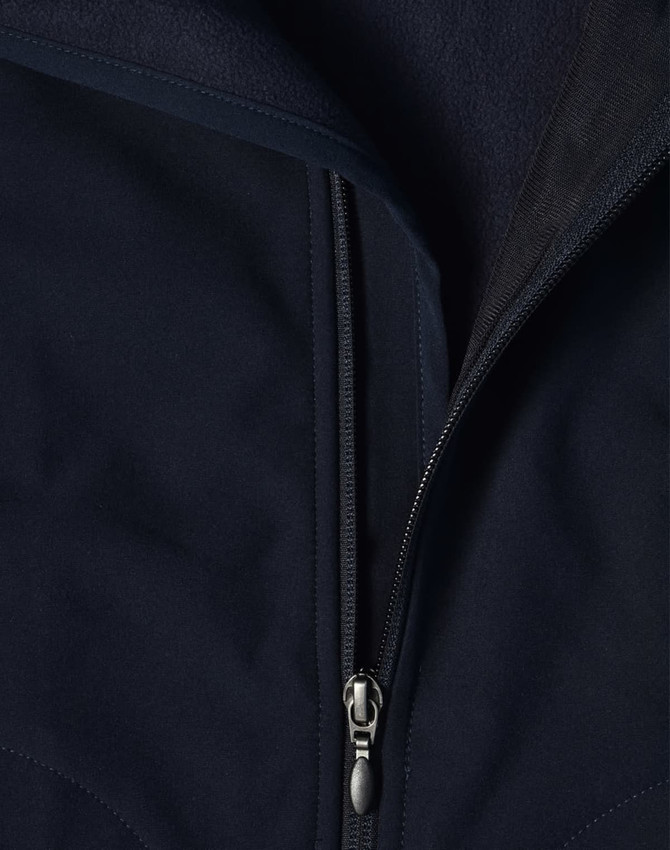 A close-up of a navy softshell vest featuring a zippered front and a fleece lining. The vest has a logo on it.