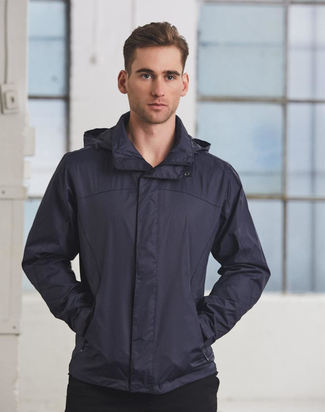 A man wearing a navy versatile jacket, standing with hands in pockets against a backdrop of large windows.