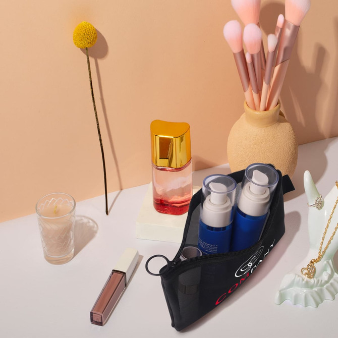A black nylon mesh flat cosmetic bag with blue and gold bottles inside, alongside makeup brushes and other beauty items.